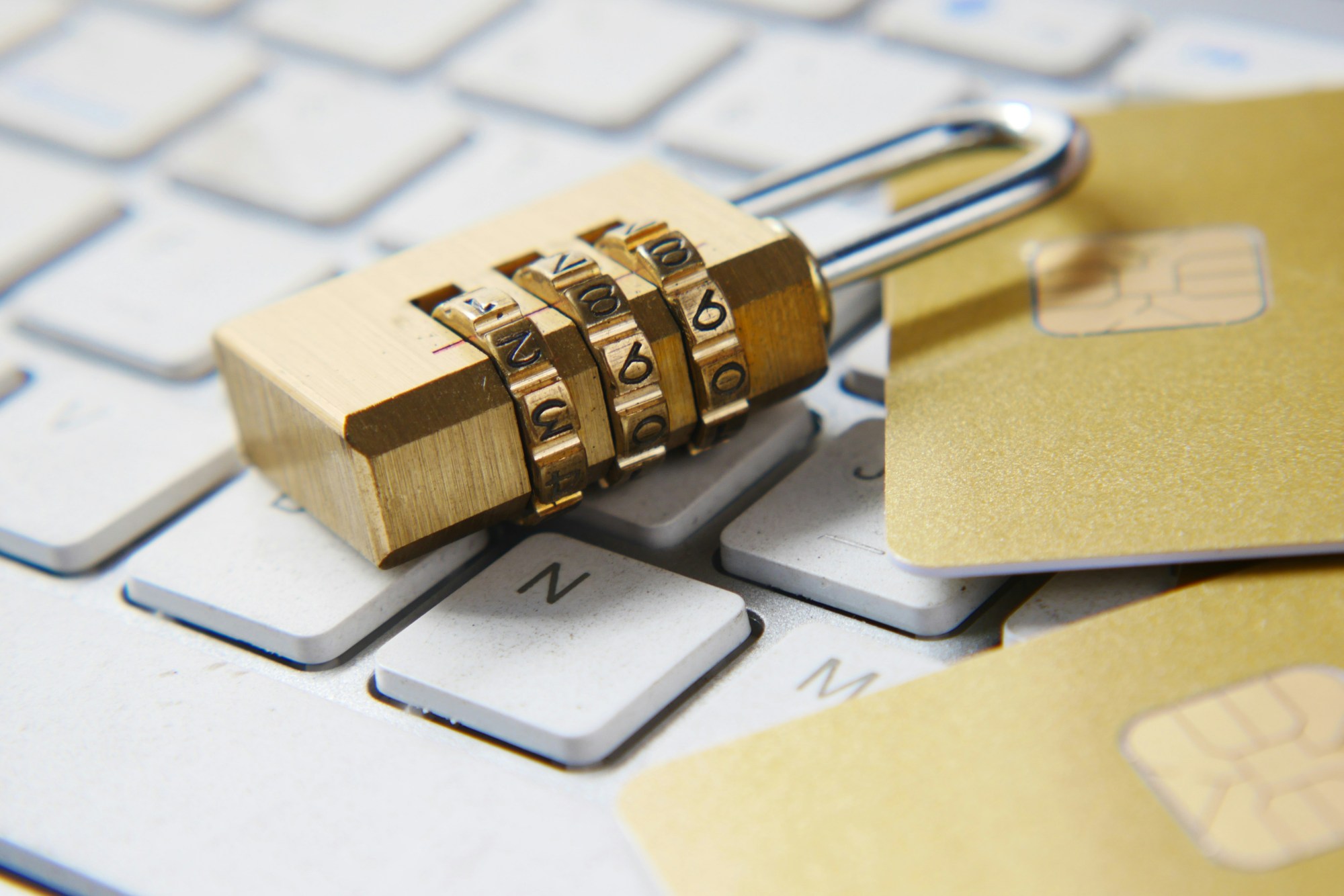 A lock and gold credit cards on a white computer keyboard.